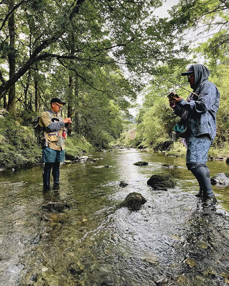 木々に囲まれた川で釣りをする2人のアングラー